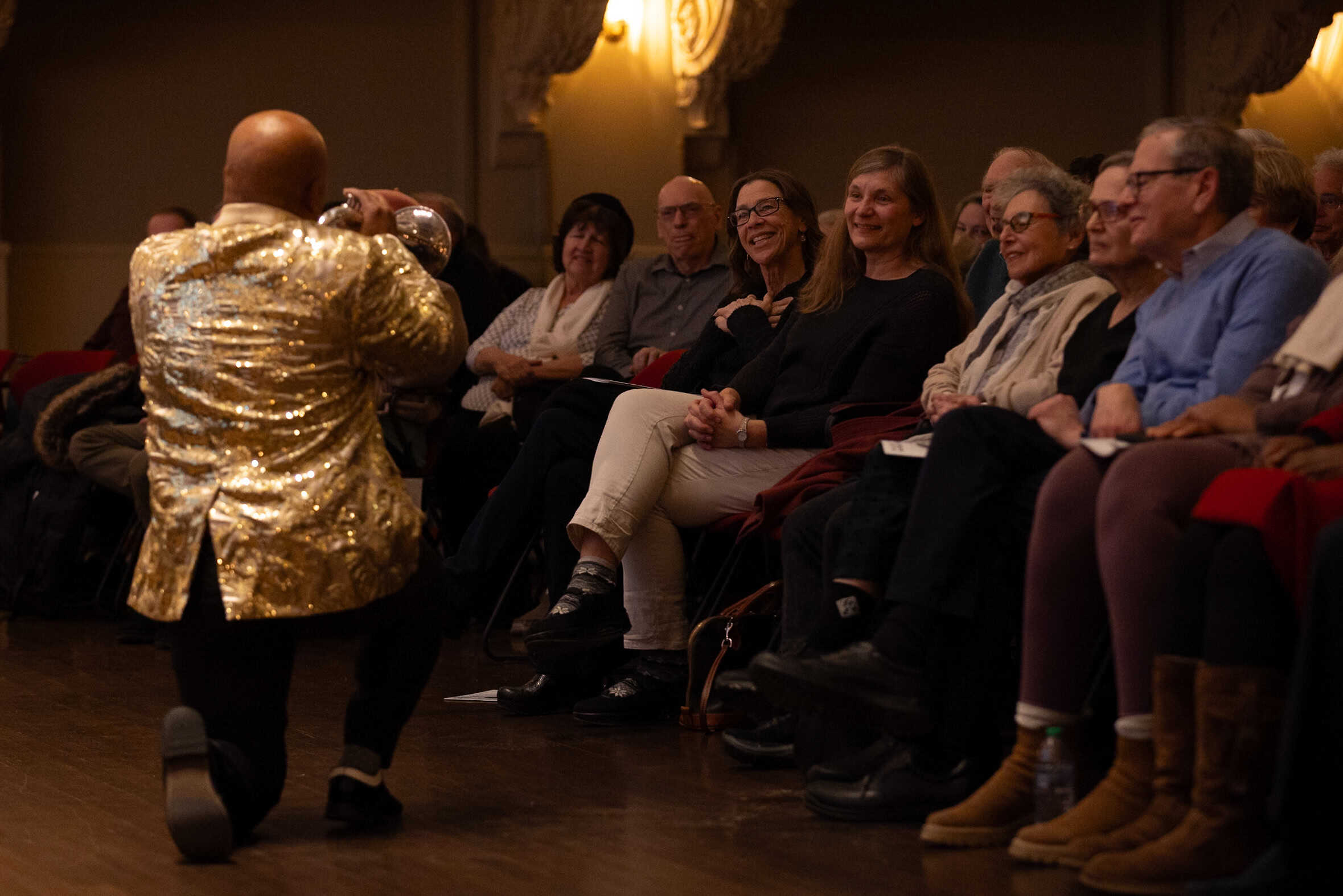 A trumpet player, seen from behind, playing for a row of audience members