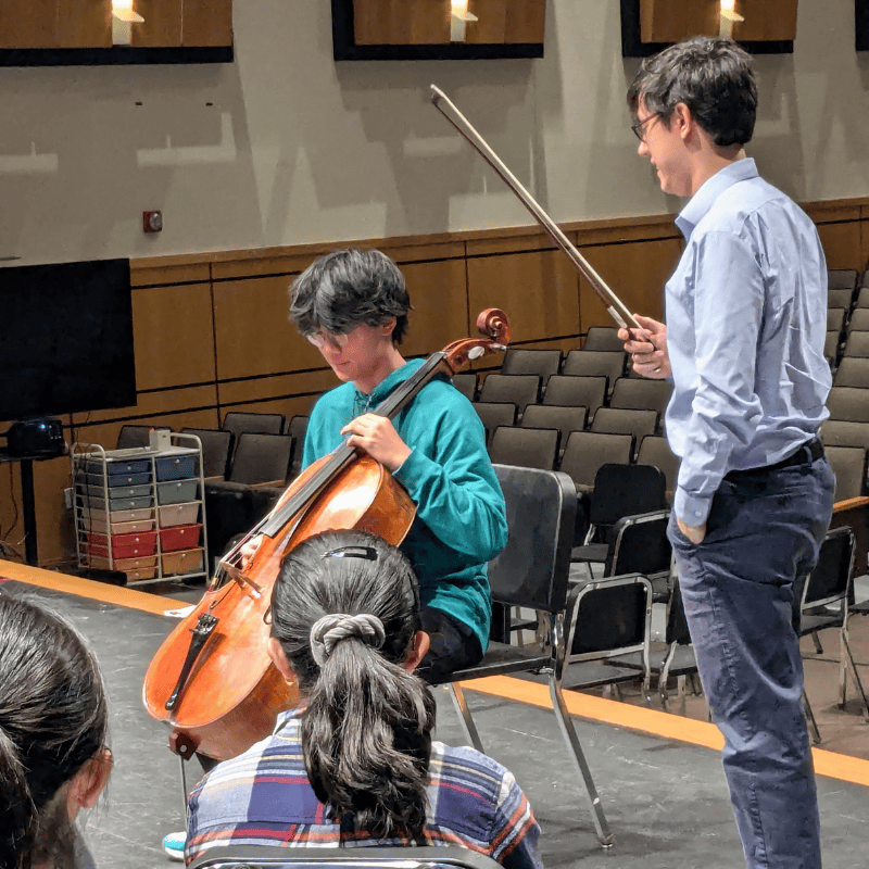 5 A student playing a cello with an instructor standing near by