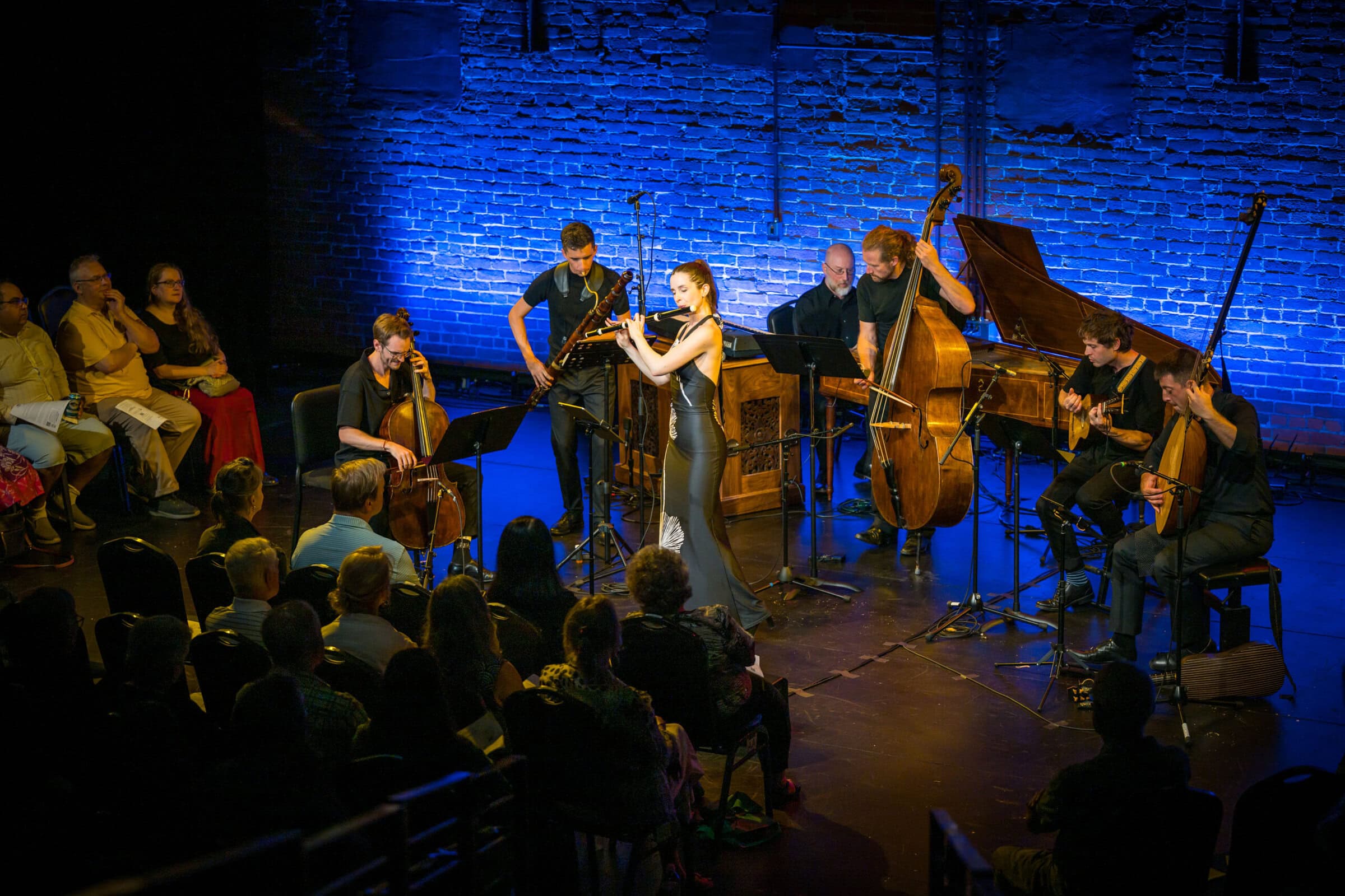 A flute player and several other musicians on stage against a blue background.